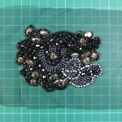 Aplicação decorativa com contas e pedras em fundo preto sobre superfície verde quadriculada