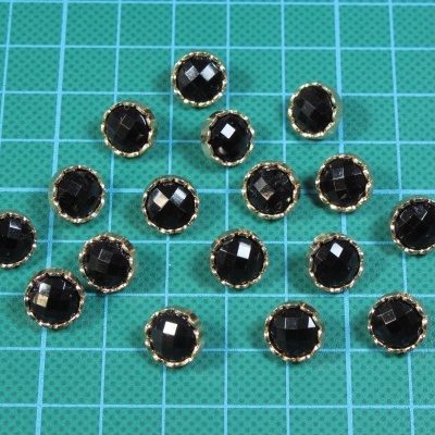 Botões redondos pretos com borda dourada sobre fundo quadriculado verde