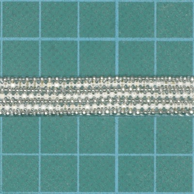 Fita decorativa prateada com padrão entrelaçado sobre fundo verde quadriculado