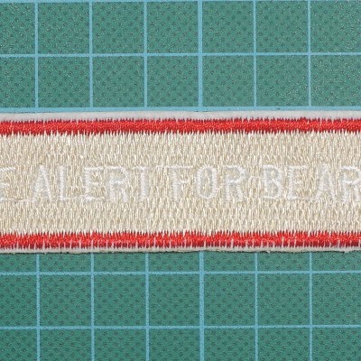 Patch bordado com texto 'BE ALERT FOR BEARS' sobre superfície verde de corte