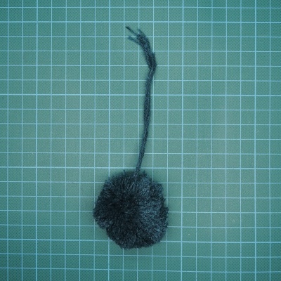 Pompom negro com cordão sobre superfície quadriculada verde