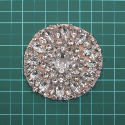 Broche redondo com cristais transparentes em padrão simétrico sobre suporte metálico dourado