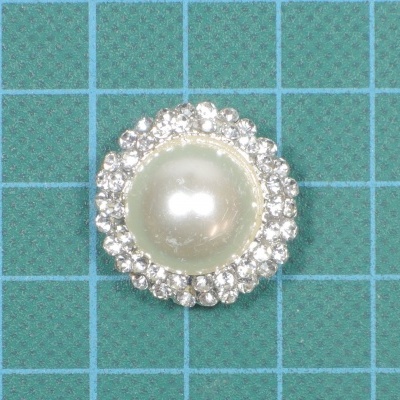 Botão redondo com pérola e cristais sobre tecido verde quadriculado azul