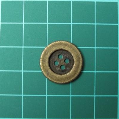 Botão metálico dourado com quatro furos sobre superfície verde com grelha branca