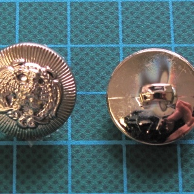 Dois botões metálicos prateados, um com relevo e outro com fecho, sobre superfície quadriculada azul.