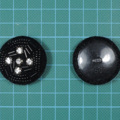 Dois botões pretos redondos, um com pedras brilhantes, ambos numa superfície quadriculada azul