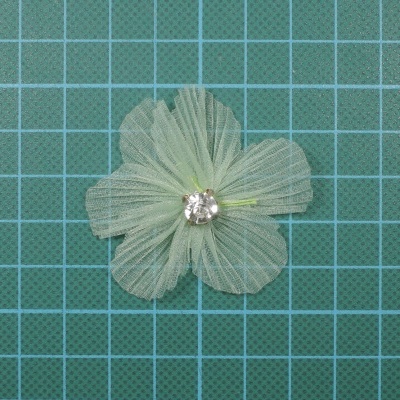 Flor decorativa verde claro em tecido com pedra brilhante no centro sobre superfície verde quadriculada