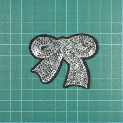 Laço decorativo preto com lantejoulas prateadas sobre superfície verde quadriculada