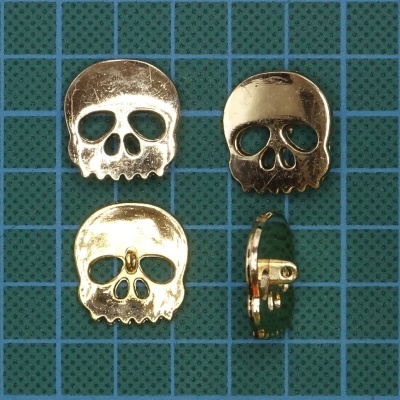 Botões metálicos dourados em formato de caveira sobre fundo quadriculado verde e azul