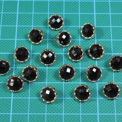 Botões pretos facetados com borda dourada sobre superfície quadriculada
