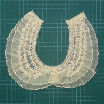 Gola de renda branca com bordados florais sobre superfície quadriculada verde