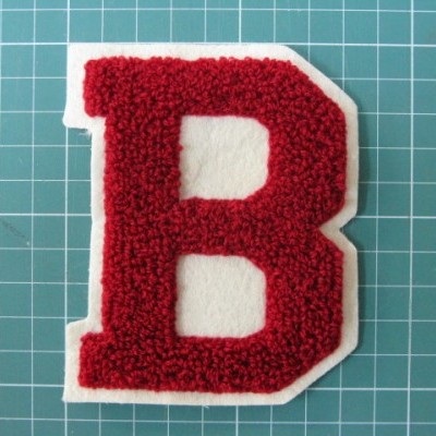 Aplicação em forma de letra B vermelha felpuda sobre base branca e tapete de corte verde