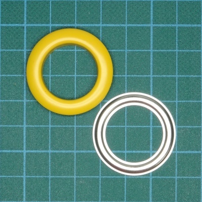 Dois anéis, um amarelo e outro metálico prateado sobre superfície de corte verde quadriculada