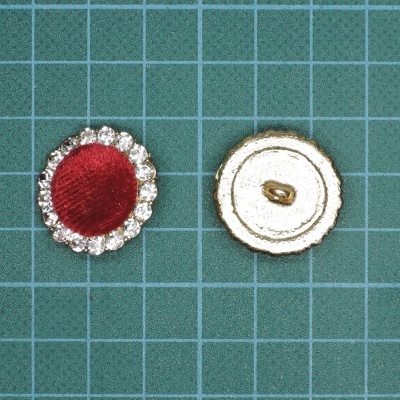 Dois botões decorativos circulares, um vermelho com borda prateada e outro branco creme com borda dourada sobre fundo verde quadriculado