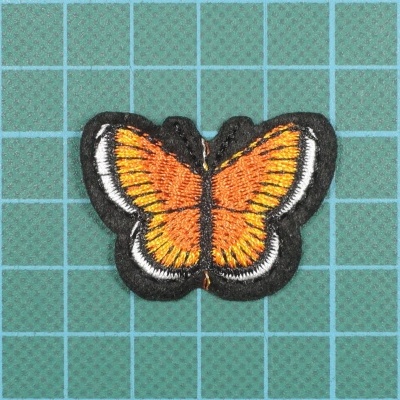 Aplicação bordada em forma de borboleta sobre fundo verde quadriculado