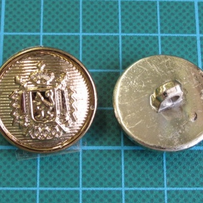 Dois botões dourados com brasão e fecho, sobre fundo de grade azul