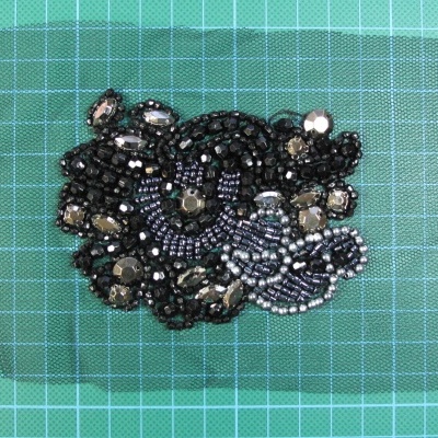 Acessório artesanal com contas e lantejoulas em padrão floral sobre rede transparente