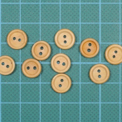 Dez botões de madeira clara com dois orifícios sobre superfície quadriculada verde