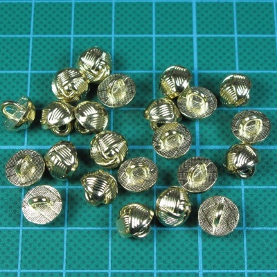 Botões metálicos dourados com padrão estriado sobre tapete verde quadriculado