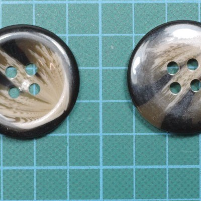 Dois botões redondos marmoreados em preto, bege e branco sobre fundo de grade azul clara