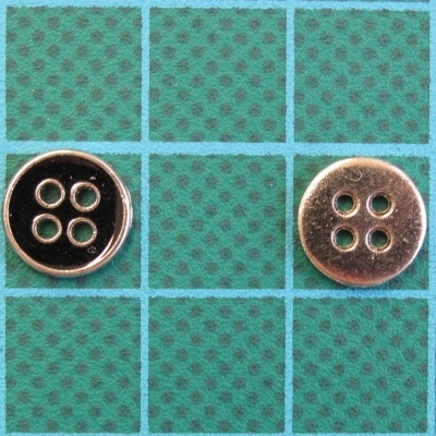 Dois botões metálicos redondos com quatro buracos sobre superfície quadriculada verde