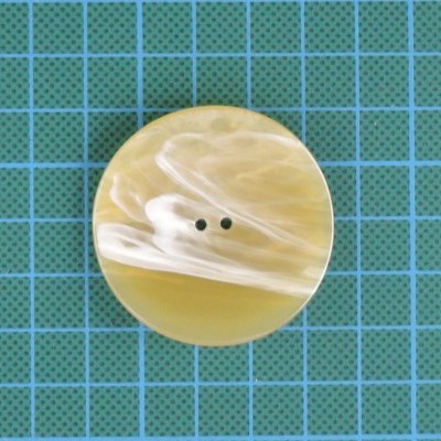 Botão redondo bege e branco com dois furos sobre fundo azul quadriculado