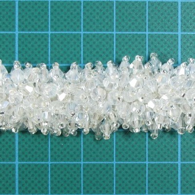 Pulseira de cristais transparentes e bagas brancas sobre fundo azul quadriculado