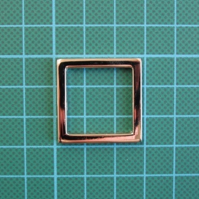 Argola quadrada metálica dourada sobre superfície verde quadriculada