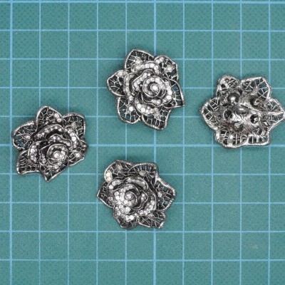 Quatro botões flor metálicos sobre fundo azul com grade branca.