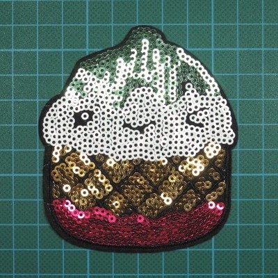 Aplicação de cupcake com lantejoulas brancas, douradas e vermelhas sobre fundo quadriculado verde