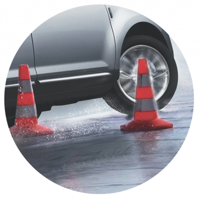 Carro prateado entre cones de trânsito laranja em superfície molhada