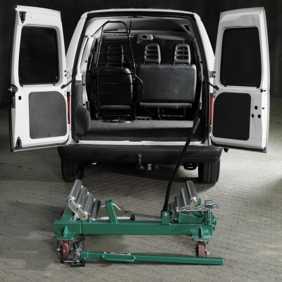 Carrinha branca com portas traseiras abertas e equipamento metálico verde no chão.