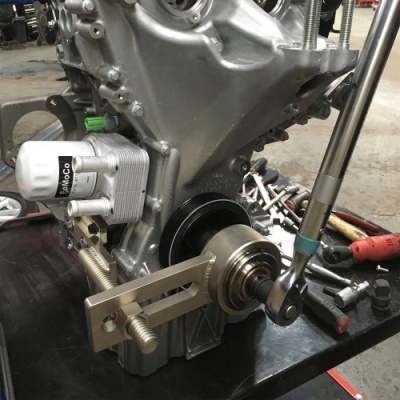 Motor de automóvel com filtro de óleo branco e chave inglesa numa bancada preta