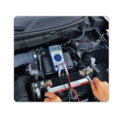 Multímetro digital a medir voltagem numa bateria de carro no compartimento motor