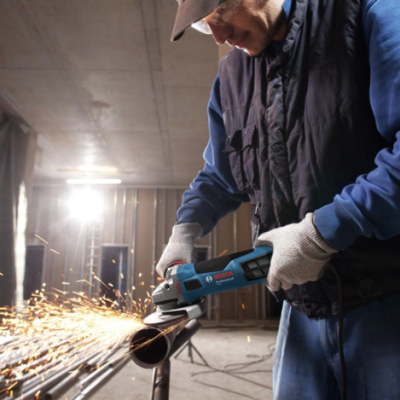 Homem a cortar tubo metálico com rebarbadora Bosch numa oficina.