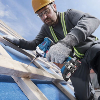 Parafusadeira Bosch azul com trabalhador em capacete e luvas numa construção de madeira