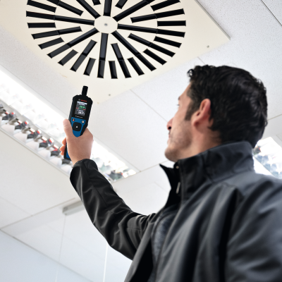 Pessoa segurando dispositivo digital Bosch num teto interior com iluminação e grelha de ventilação
