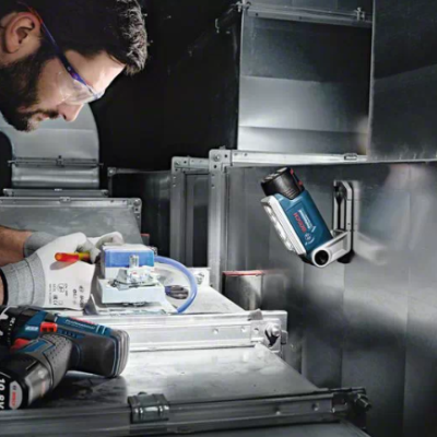 Homem a usar ferramentas Bosch num ambiente industrial com tubos metálicos.