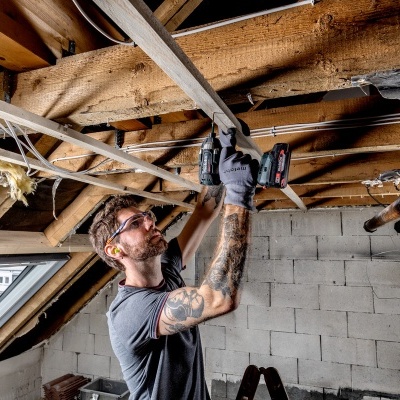 Homem a instalar isolamento térmico num sótão com teto de madeira e parede de blocos