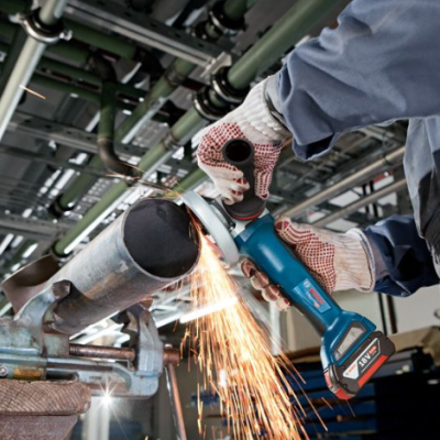 Pessoa a cortar tubo metálico com rebarbadora azul em ambiente industrial
