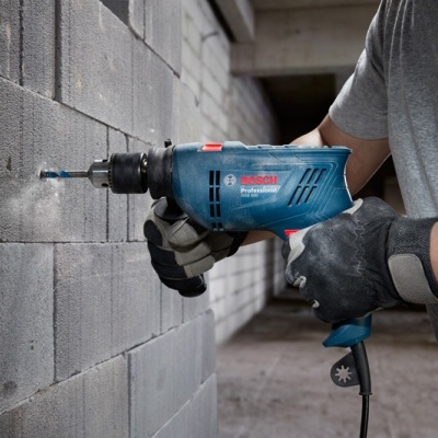 Pessoa usando furadeira elétrica Bosch Professional azul para furar parede de blocos de cimento cinza