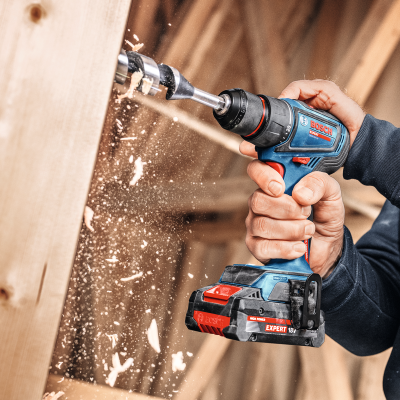 Perfuração em madeira com serra Bosch Expert 18V azul e preta nas mãos de uma pessoa