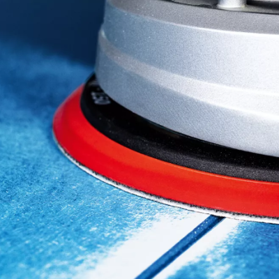 Lixadeira elétrica prateada com disco laranja sobre superfície azul