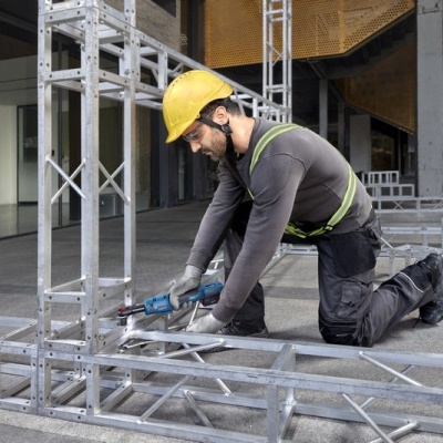 Homem a trabalhar com ferramenta elétrica em estrutura metálica prateada num canteiro de obras