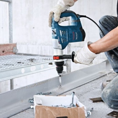 Pessoa a usar furadeira elétrica azul para perfurar metal cinzento com caixa de parafusos.