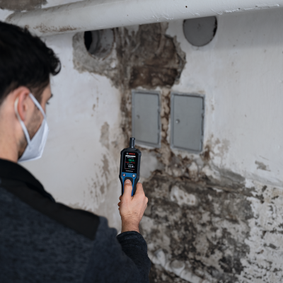 Medidor digital Bosch Professional preto e azul em mãos num ambiente interior com paredes mofadas