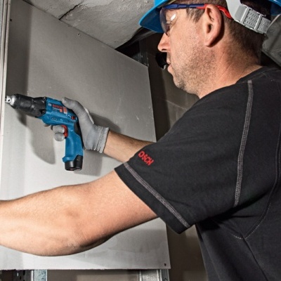 Homem com capacete azul a usar parafusadeira em ambiente de construção