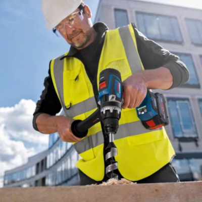 Homem a usar furadeira azul em obra com colete amarelo e capacete branco
