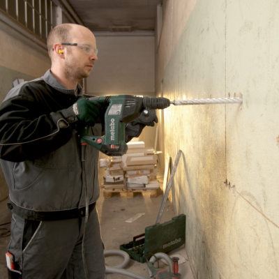 Homem a usar furadeira Metabo para perfurar parede numa área de construção