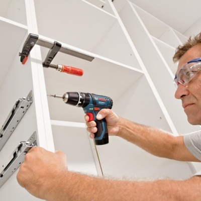 Homem a montar móvel branco com furadeira eléctrica